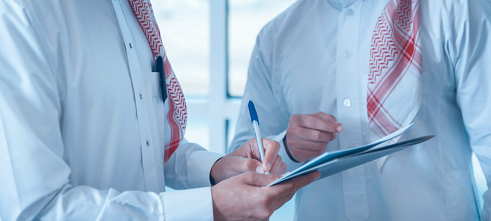 مستشاران سعوديان بالزي التقليدي يراجعات مستندات ويدونان الملاحظات على لوحة كتابة